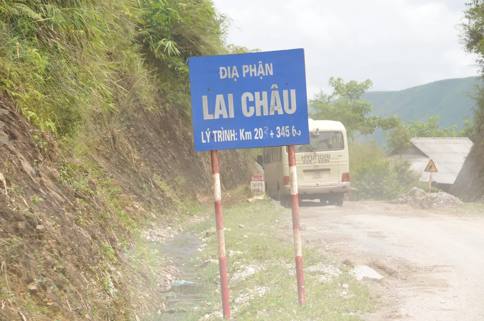 Biển báo Địa phận Lai Châu bên đường núi, phía sau là một chiếc xe khách