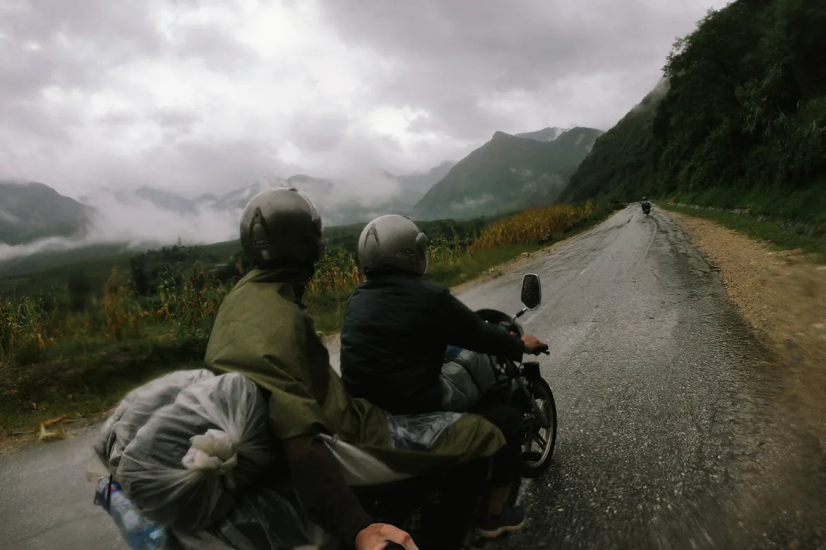 Hai người đi xe máy chở hàng trên đường núi ướt, mây phủ sườn núi ở vùng Tam Đường cũ
